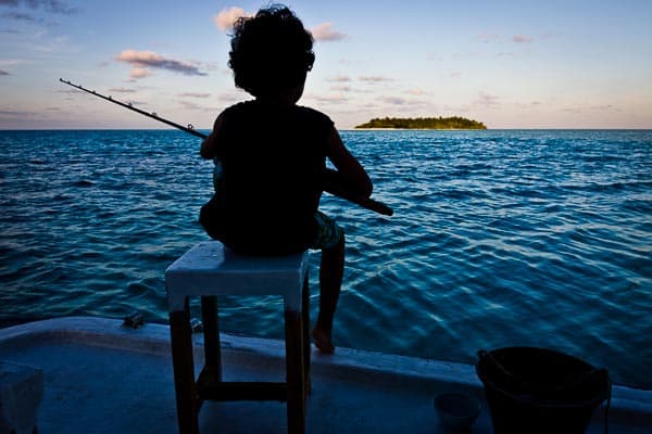Young guest fishing from the deck of NOAH at dusk, an island on the horizon