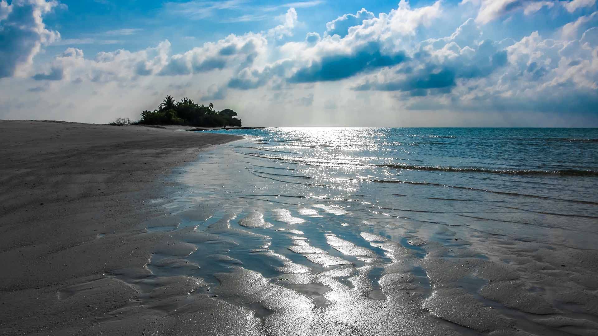 Sunlight breaking through clouds over a deserted Maldivian island and its beach